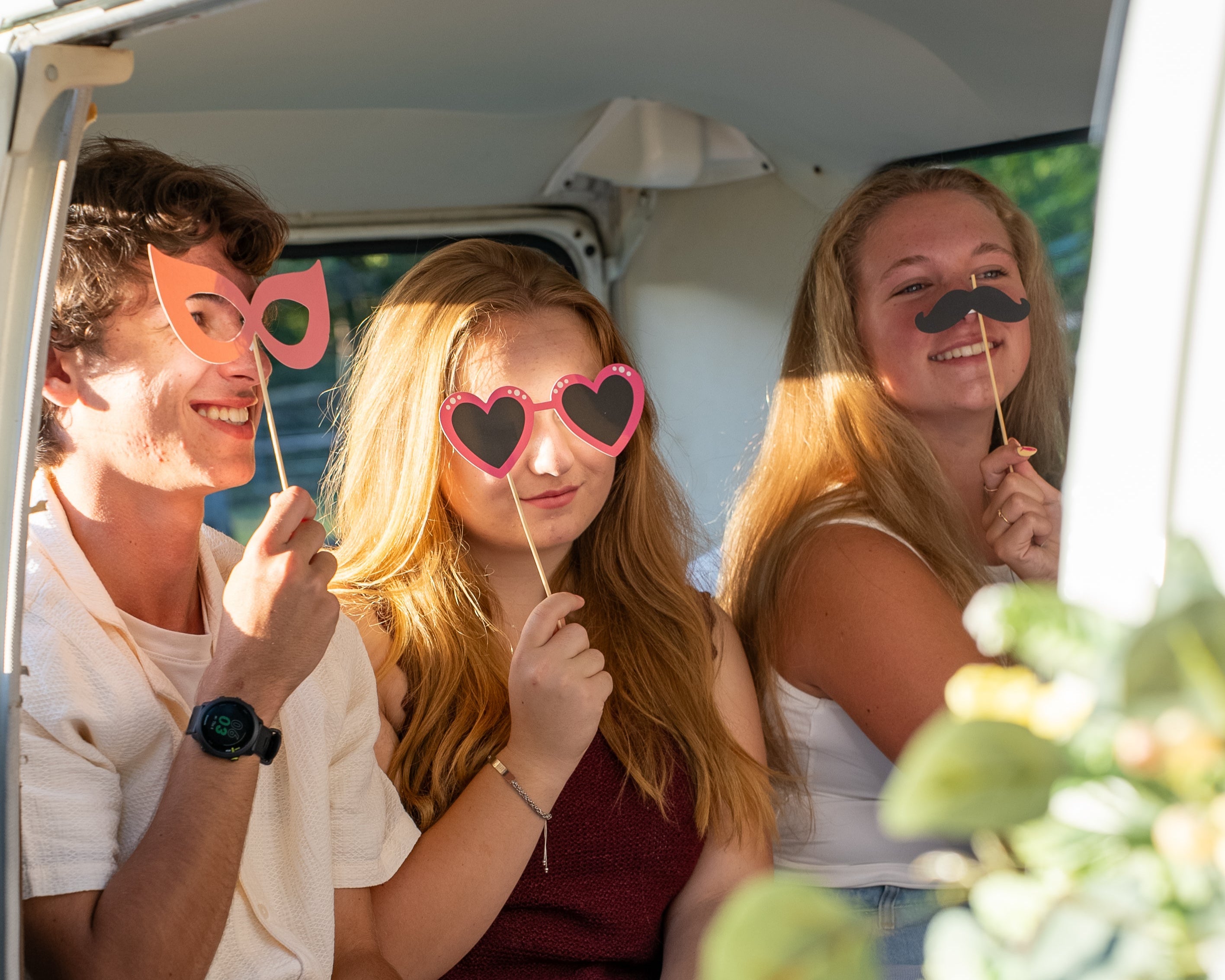 teenagers in vw photo booth bus with props held up to their faces